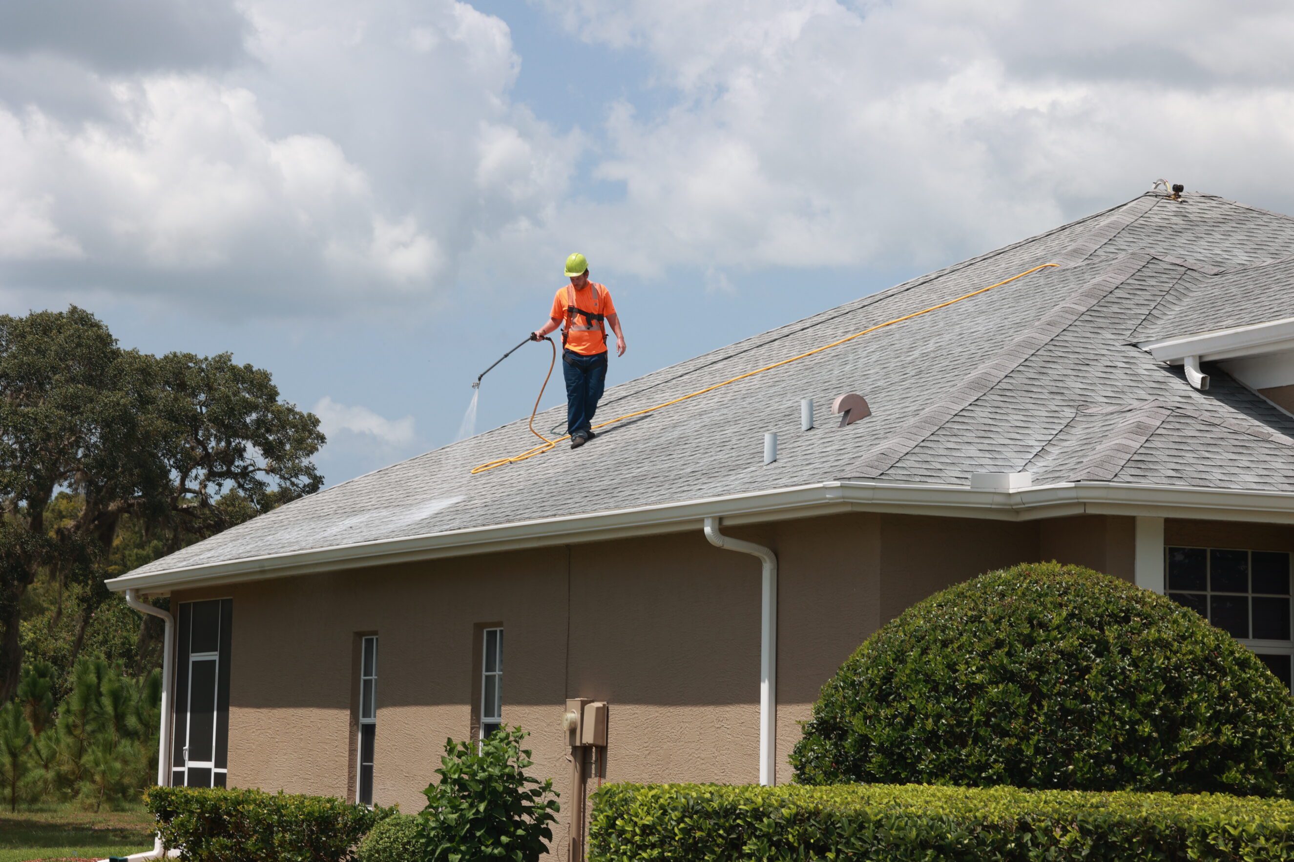 Worker pressure-washing residential roof for roof rejuvenation and home maintenance