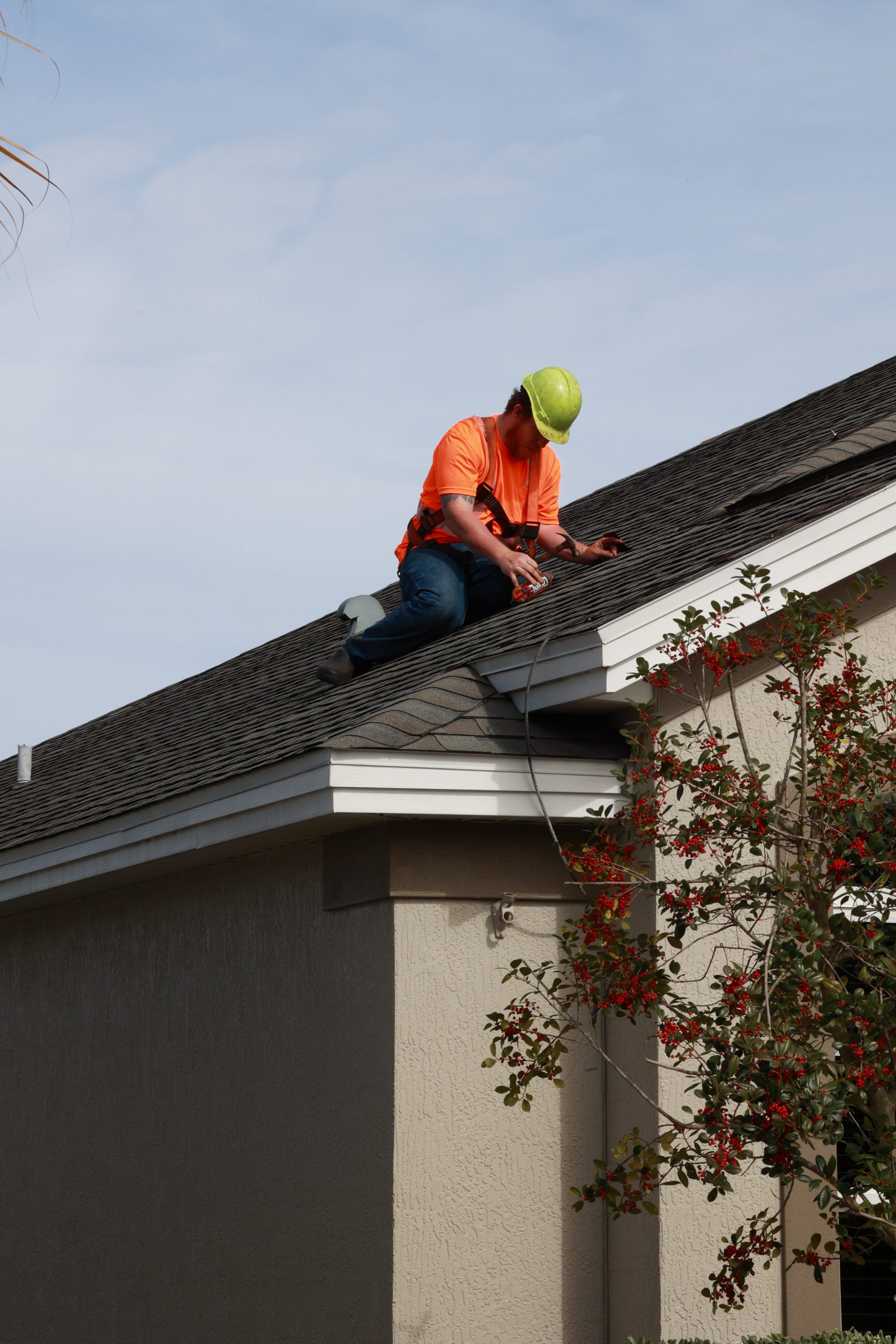 Roofer in safety gear performing roof repair on suburban home, roof rejuvenation services