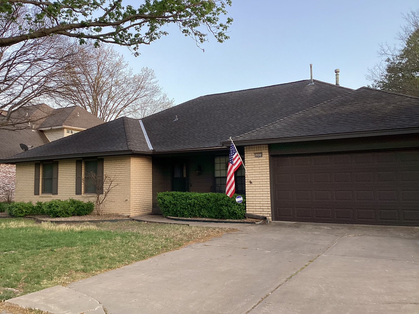Brick ranch home with dark roof, American flag by entrance, attached garage