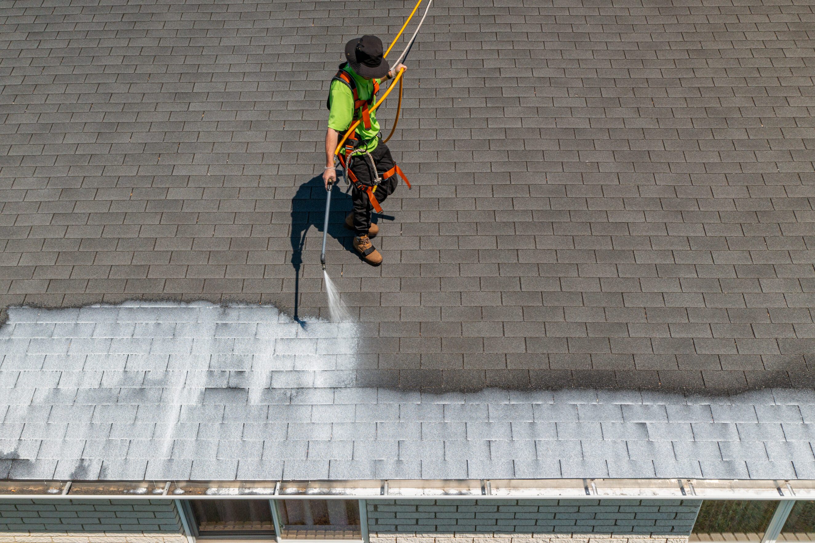 Roofer applying roof rejuvenation coating on asphalt shingles for home maintenance